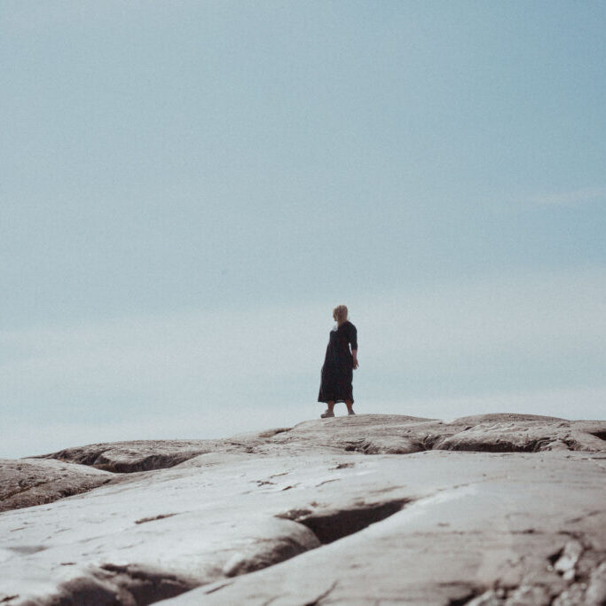 Nainen seisoo luodon päällä, katsoo sivulle auringon paistaessa ja hengittää elämää tässä ja nyt MBSR-kurssin oppien mukaan.